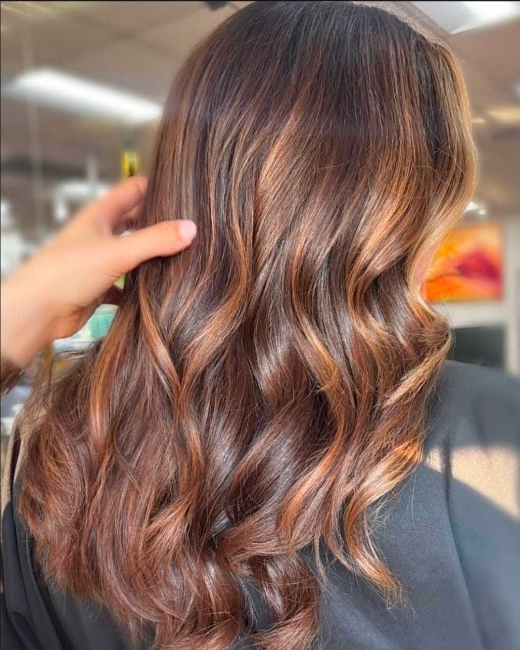 Wavy brown hair with copper highlights being styled in a salon.