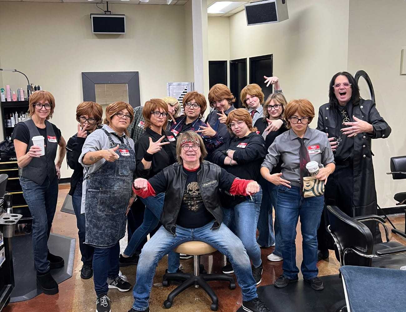 Group of people posing in a hair salon, all dressed similarly, with fun expressions.