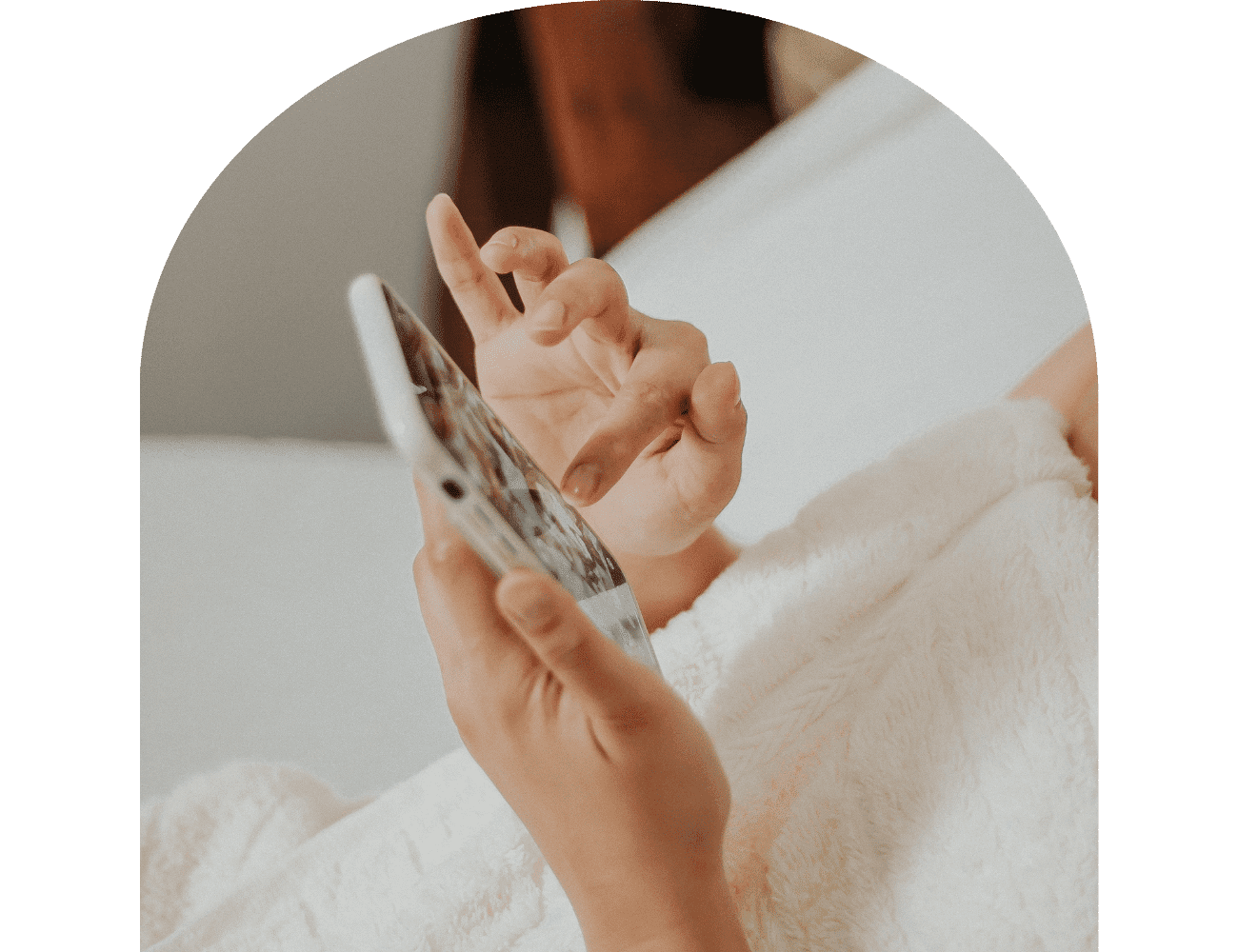 A person swipes on a smartphone while snuggled in a soft, white blanket.