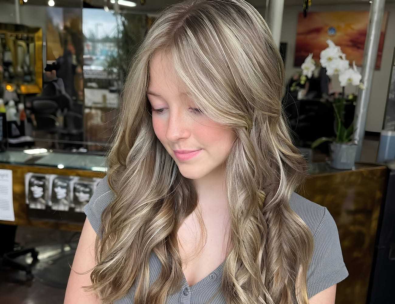 Young woman with long, wavy hair smiles in a salon setting.