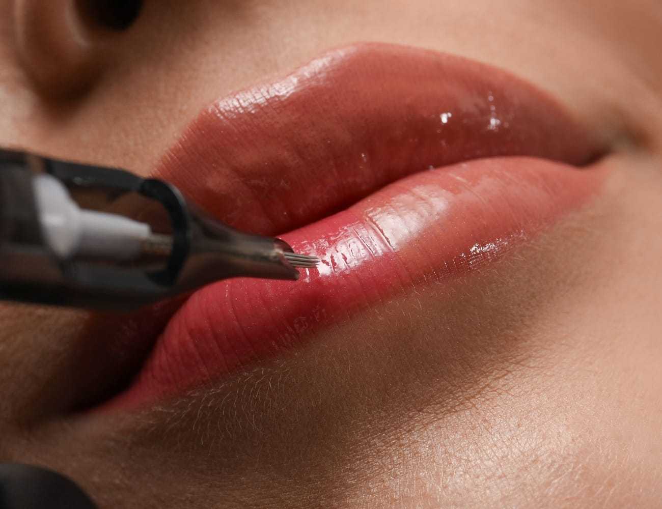 Close-up of a person’s lips being tattooed with a tool for cosmetic enhancement.